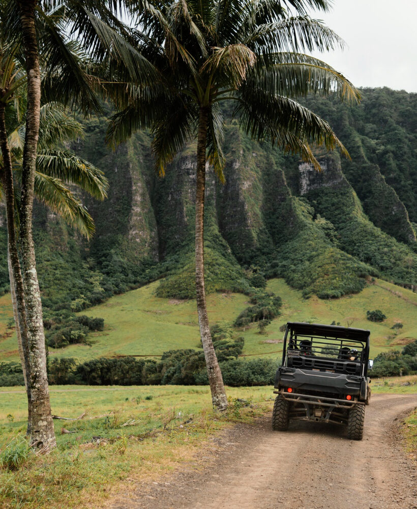 Samochód terenowy jadący szutrową drogą przez zieloną dolinę z palmami, w tle strome, porośnięte roślinnością górskie zbocza.