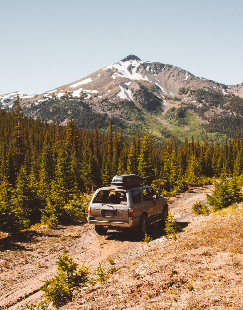 Samochód terenowy jadący szutrową drogą przez górski las z ośnieżonymi szczytami w tle