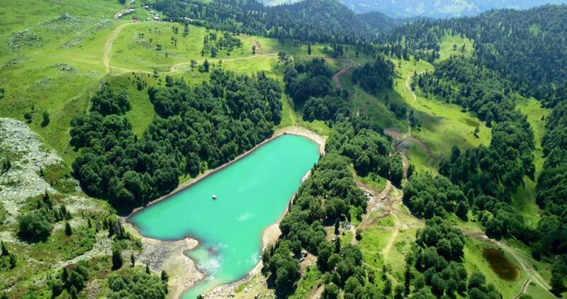Turkusowe jezioro pośród zielonych wzgórz i lasów widziane z góry