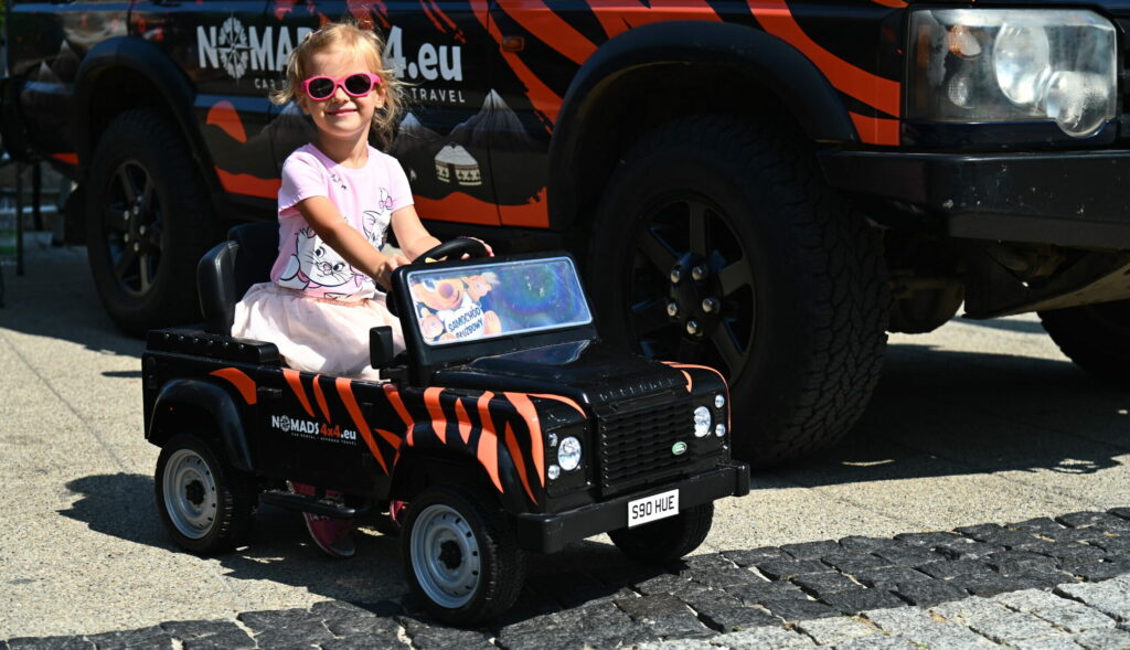 Dziecko siedzące w małym samochodzie elektrycznym zaparkowanym obok auta terenowego
