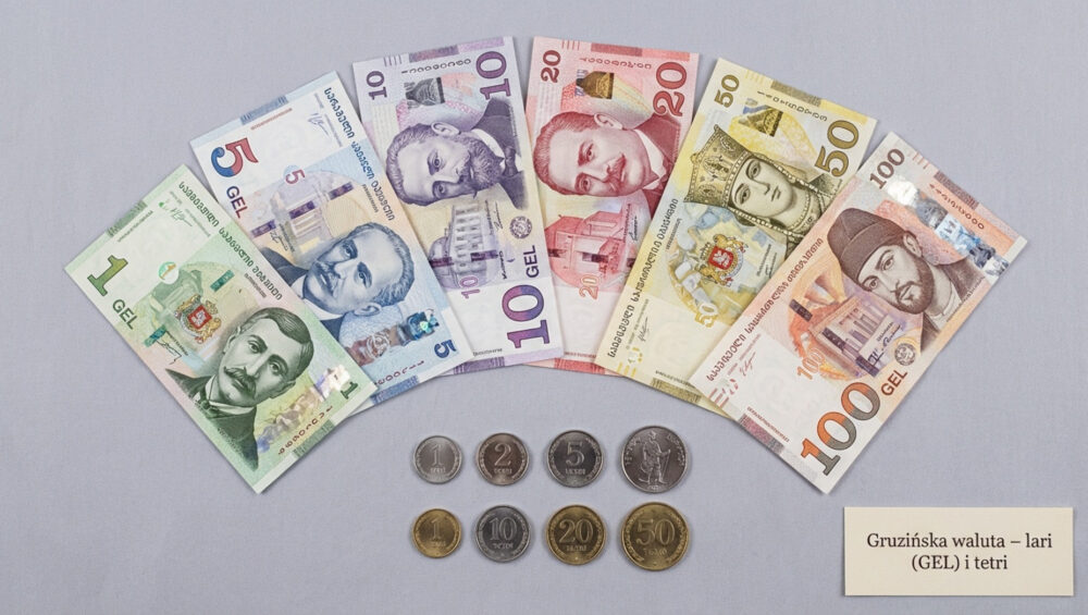 Przejrzysta fotografia banknotów i monet gruzińskiej waluty na neutralnym tle, ukazująca szczegóły i symbole narodowe.