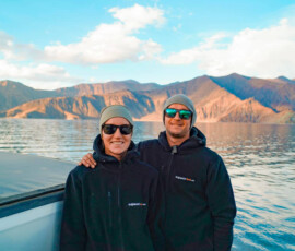 Dwie osoby stojące obok siebie nad jeziorem z górami w tle